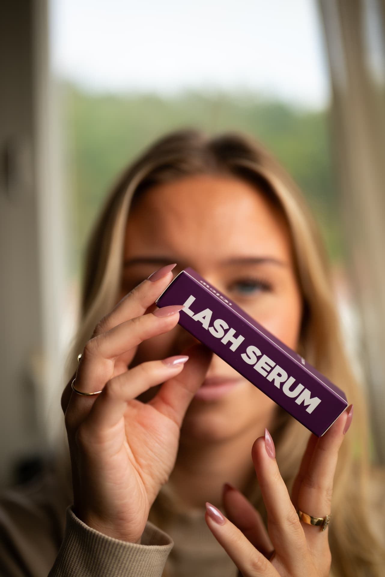 Vilde holder opp Iglow lash serum foran ansiktet